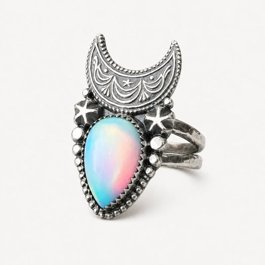 Supernova Crescent Moon Ring with luminous opal-style center on a warm white studio background